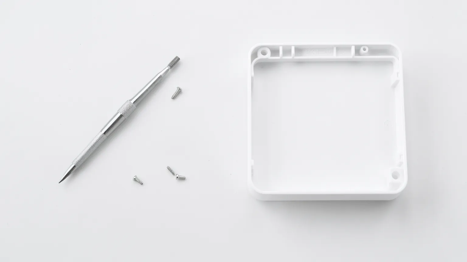 Destornillador de precisión y tornillos pequeños sobre una mesa de trabajo junto a una carcasa abierta