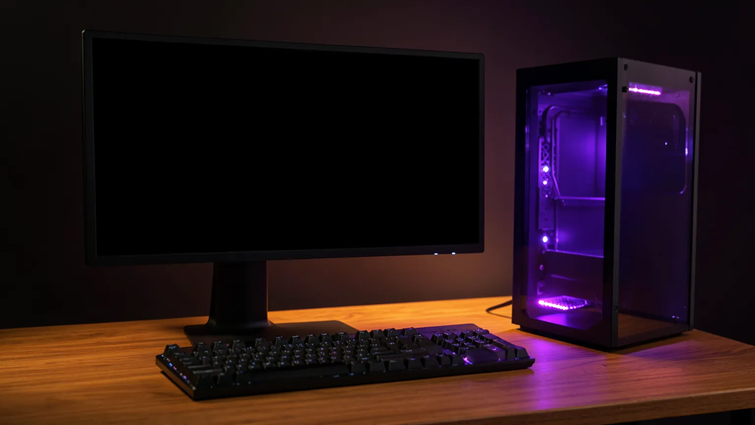 Estación de trabajo con monitor grande, teclado mecánico y torre de ordenador iluminada en violeta sobre una mesa de madera
