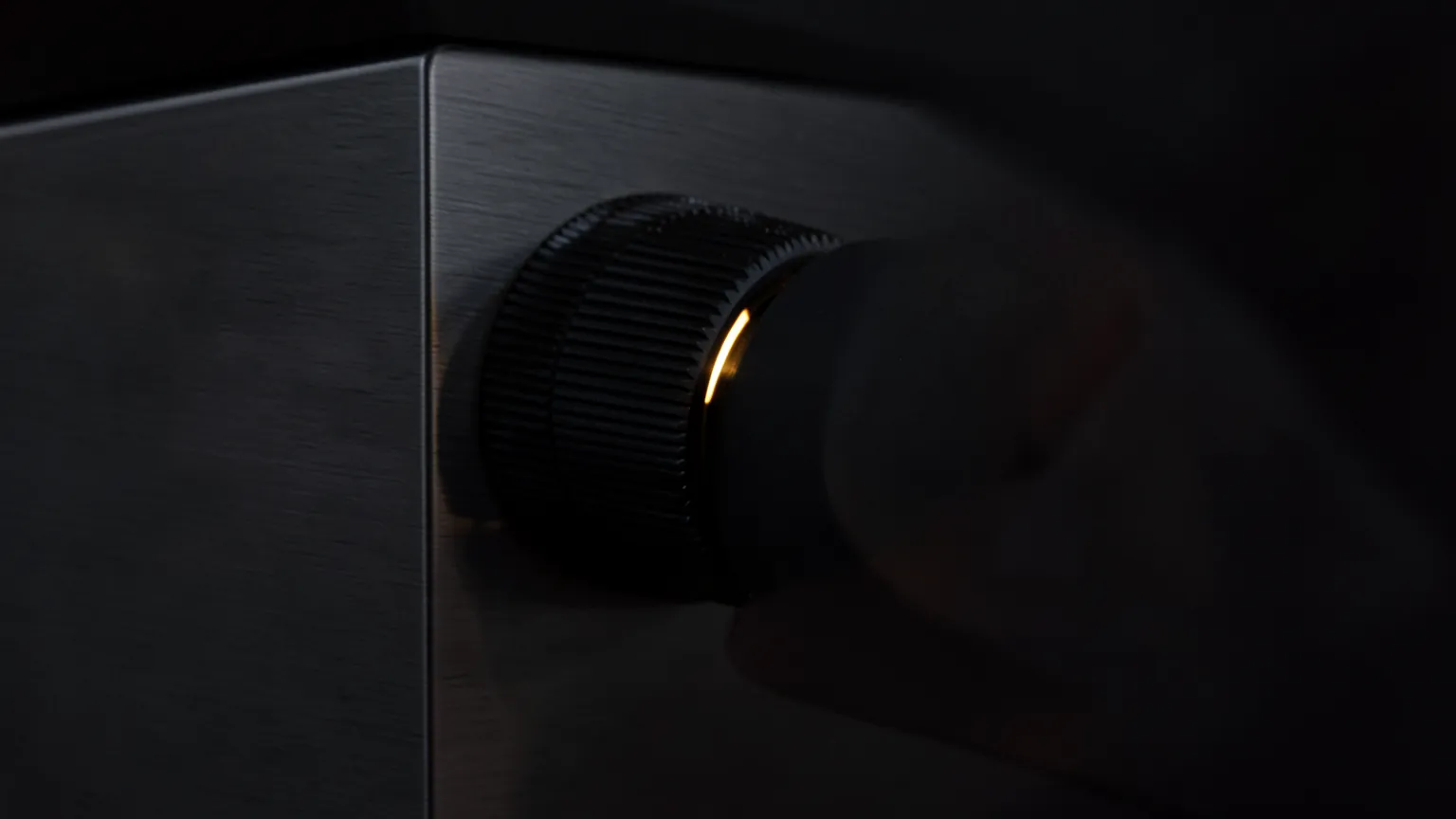 Mando giratorio metálico sobre un panel de control oscuro, iluminado por una luz cálida de canto