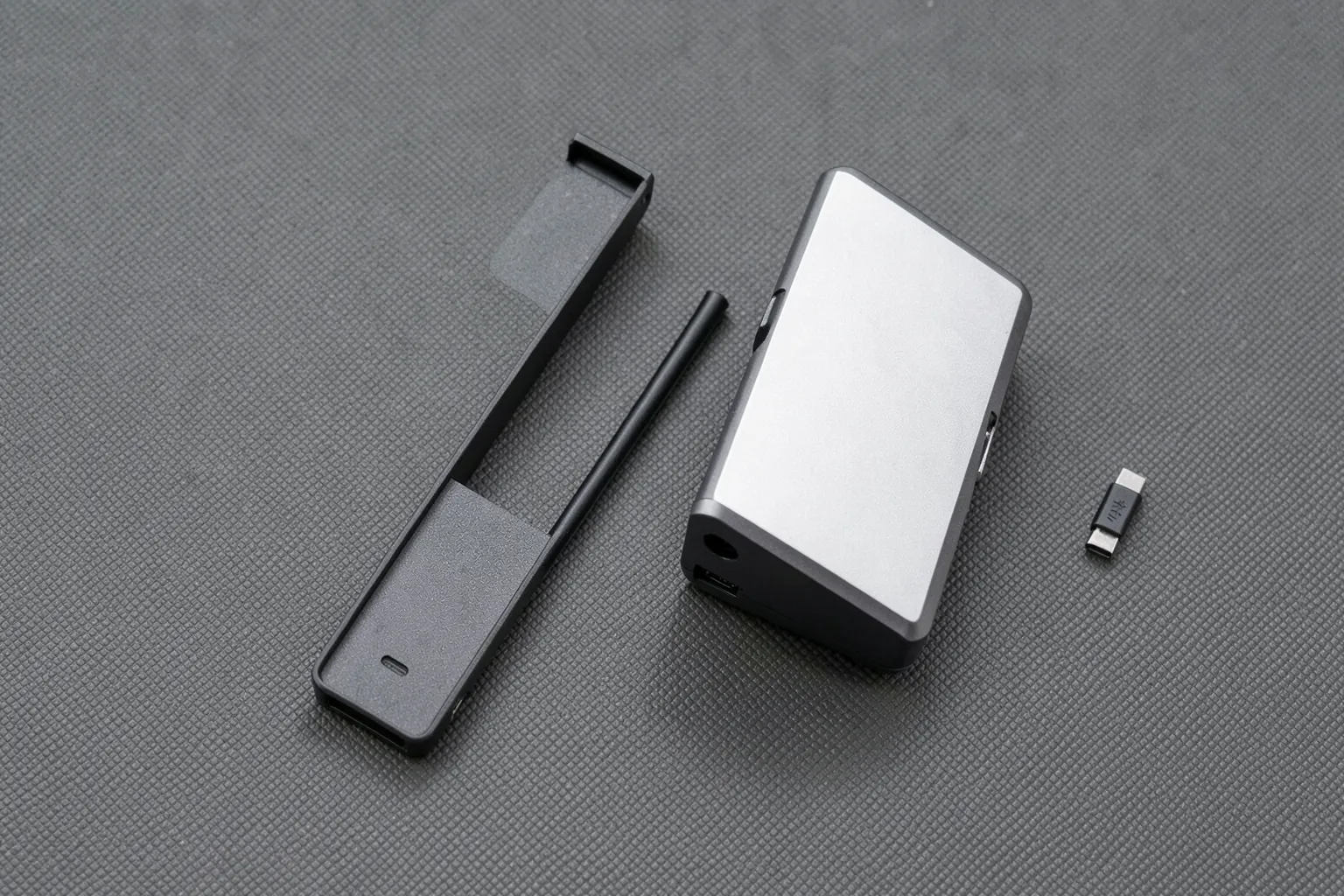 Carcasa externa alargada abierta junto a una unidad de almacenamiento y un pequeño adaptador USB-C sobre una alfombrilla gris
