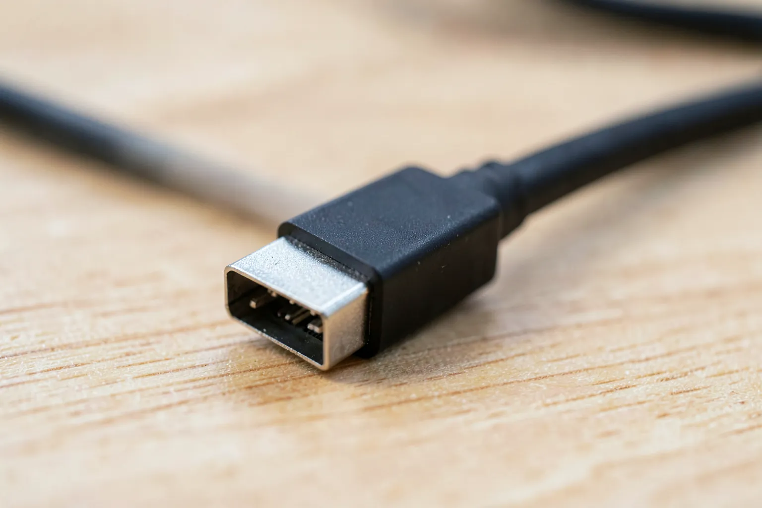 Extremo de un cable HDMI negro con el conector metálico sobre una mesa de madera clara