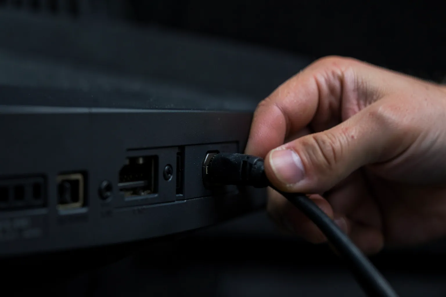 Mano conectando un cable HDMI en la parte trasera de un televisor con varias entradas