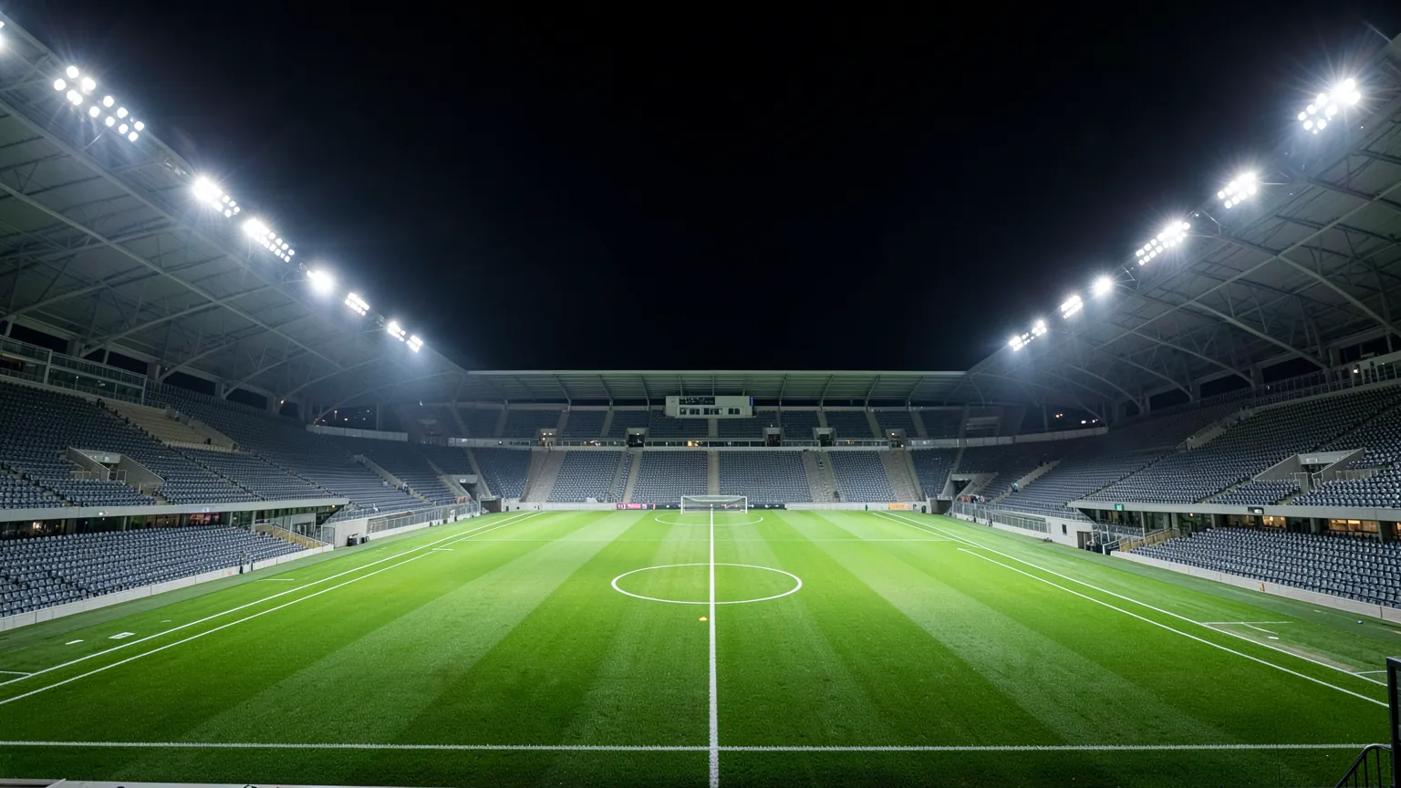 Estadio de fútbol iluminado por la noche con el césped vacío bajo los focos