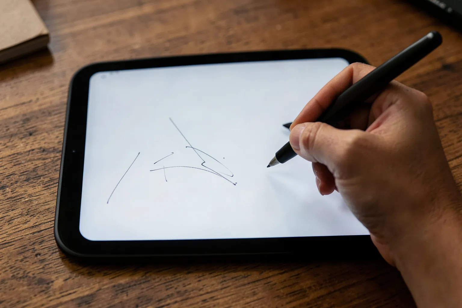 Mano escribiendo con un lápiz digital sobre una tableta de tinta electrónica grande sin marcas apoyada en un escritorio de madera