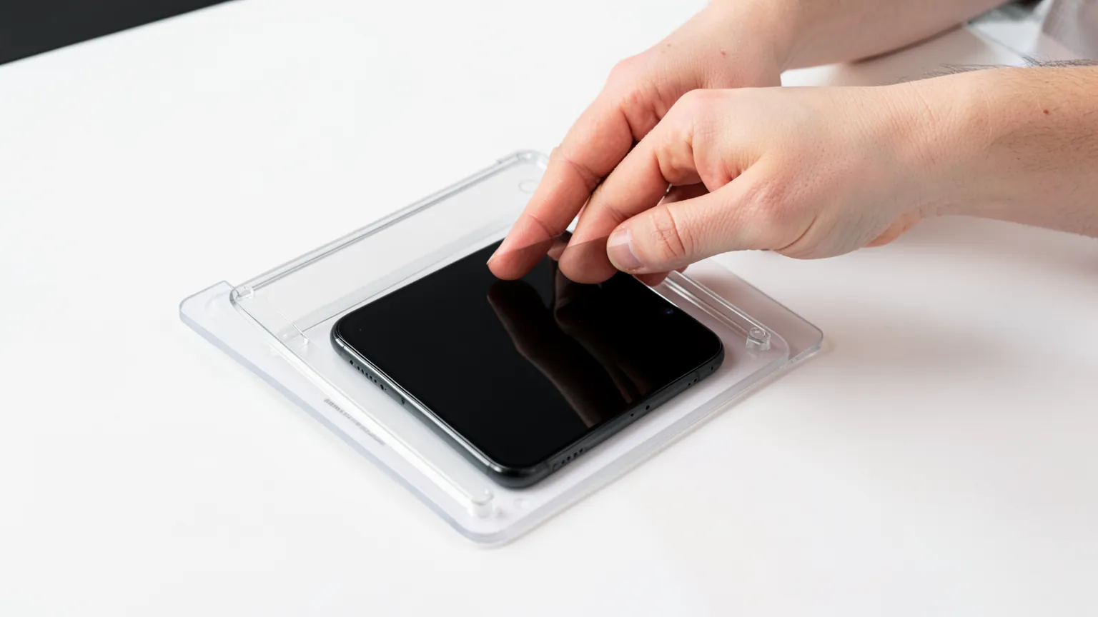 Manos colocando un protector de cristal templado sobre la pantalla de un teléfono con un marco de instalación