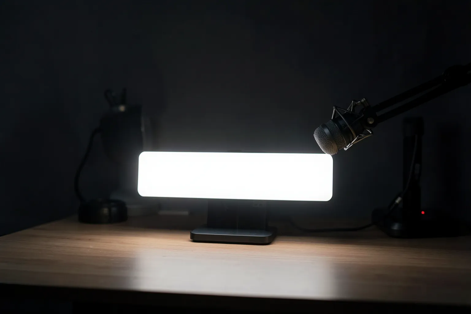 Panel de luz LED rectangular sobre un soporte de escritorio iluminando un puesto de streaming con webcam y micrófono en una habitación oscura