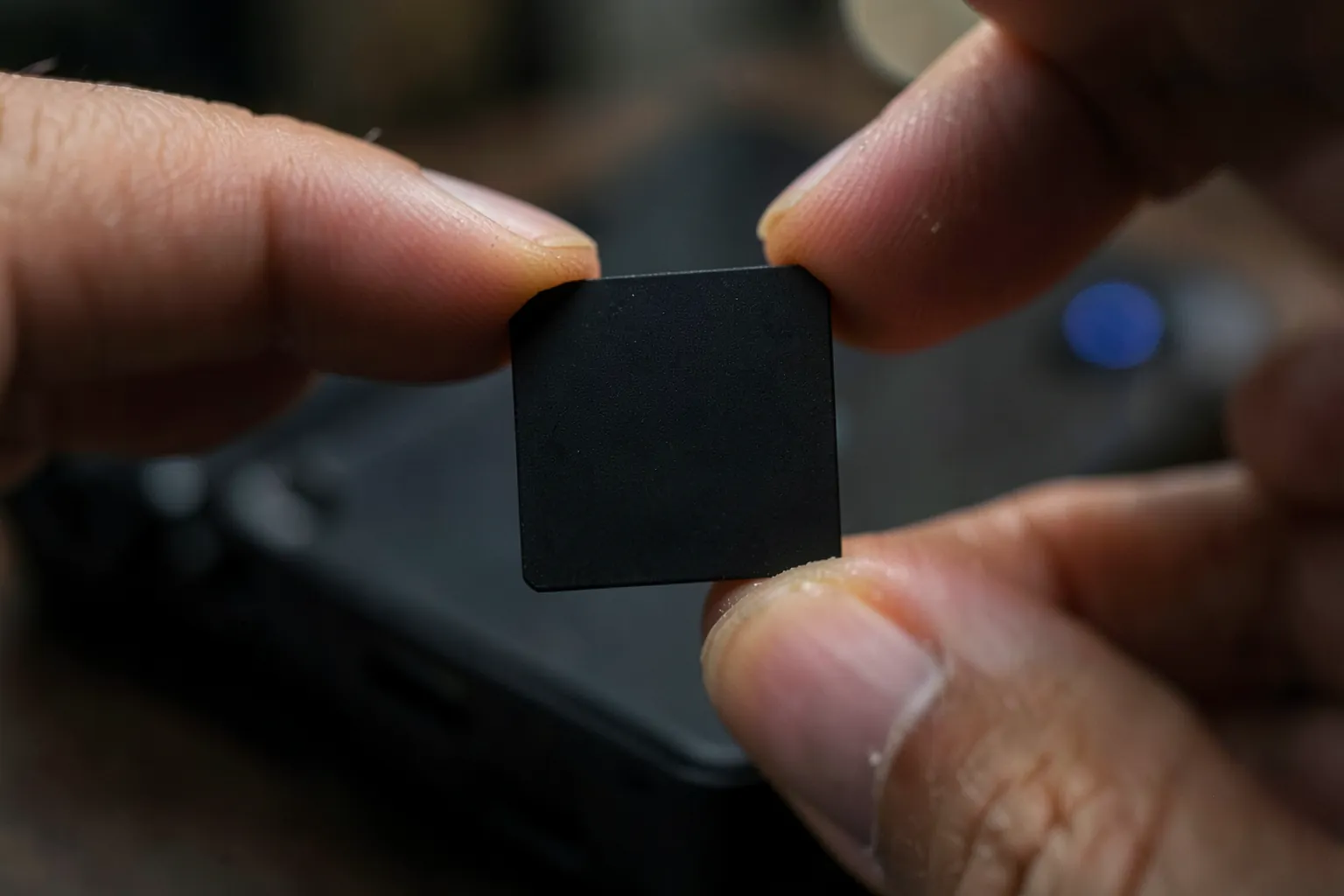 Dedos sujetando una tarjeta de memoria pequeña y negra sobre una consola portátil oscura