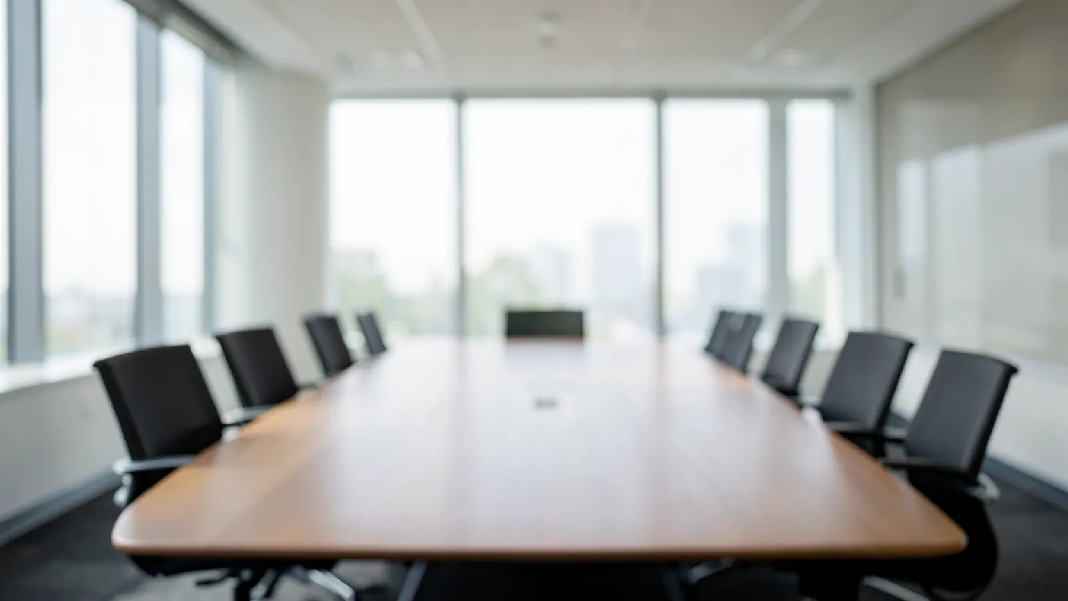 Sala de reuniones con mesa larga vacia, luz natural filtrada y pantallas apagadas