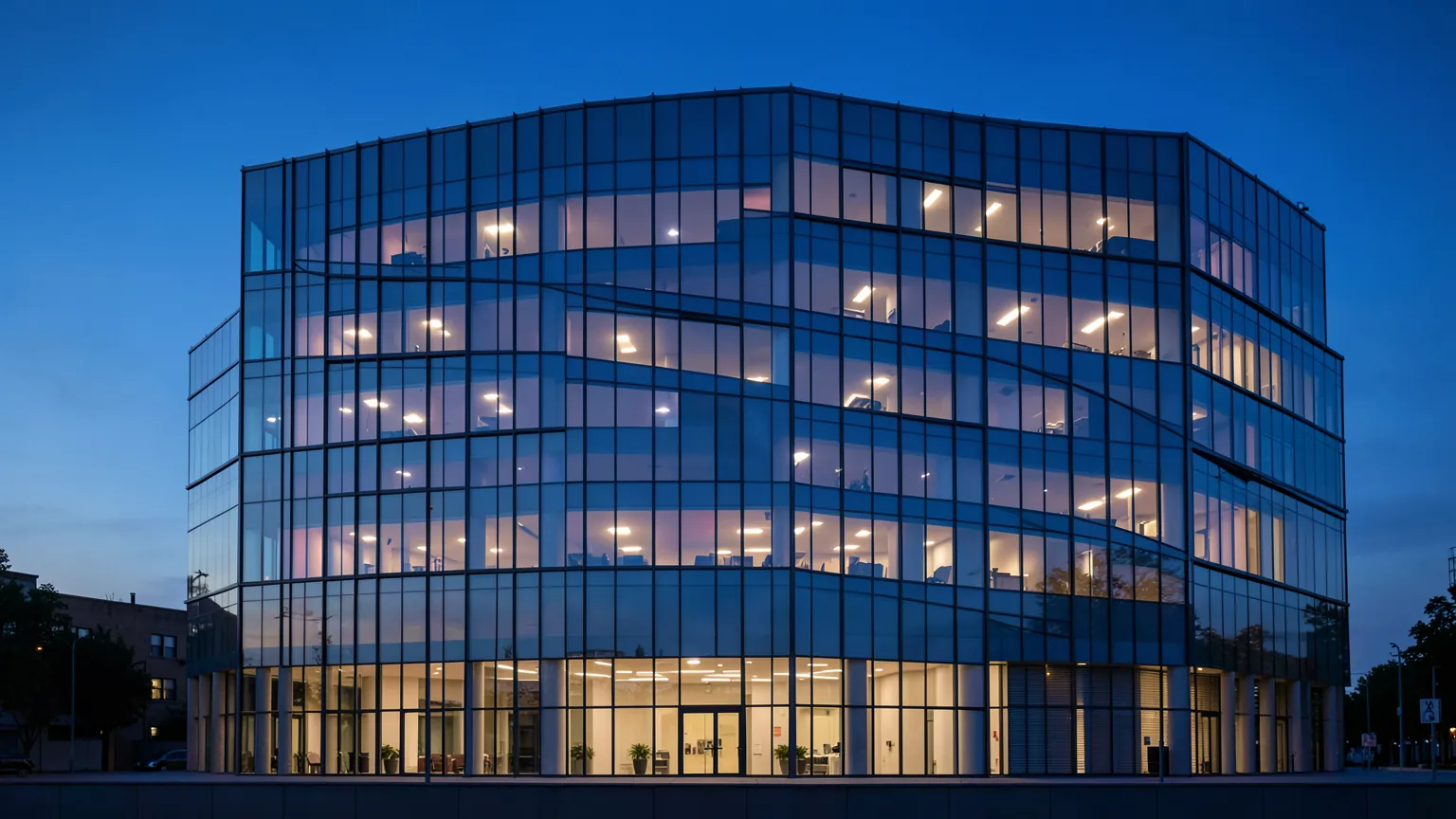 Fachada de un edificio de oficinas de cristal al anochecer con algunas ventanas iluminadas
