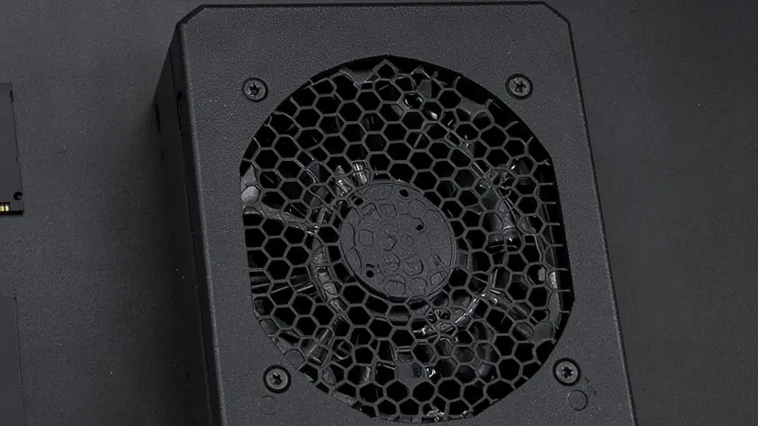 Fuente de alimentación modular negra con rejilla de ventilador sobre un banco de trabajo oscuro