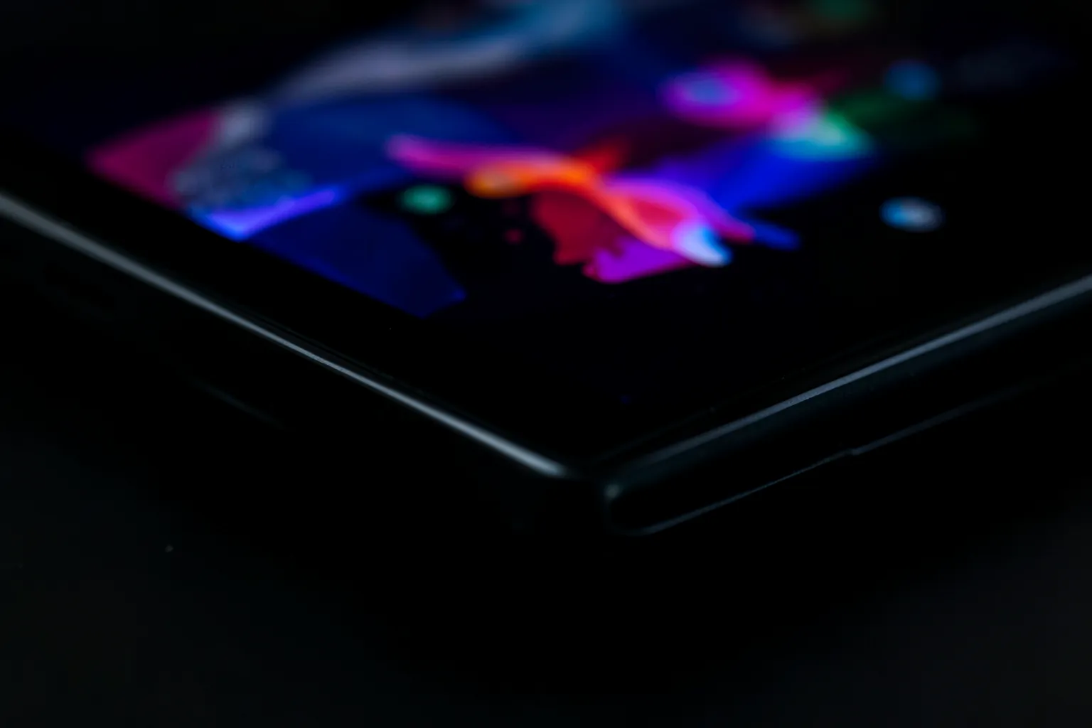Detalle del borde de una pantalla OLED de consola portátil con negros profundos y colores abstractos intensos