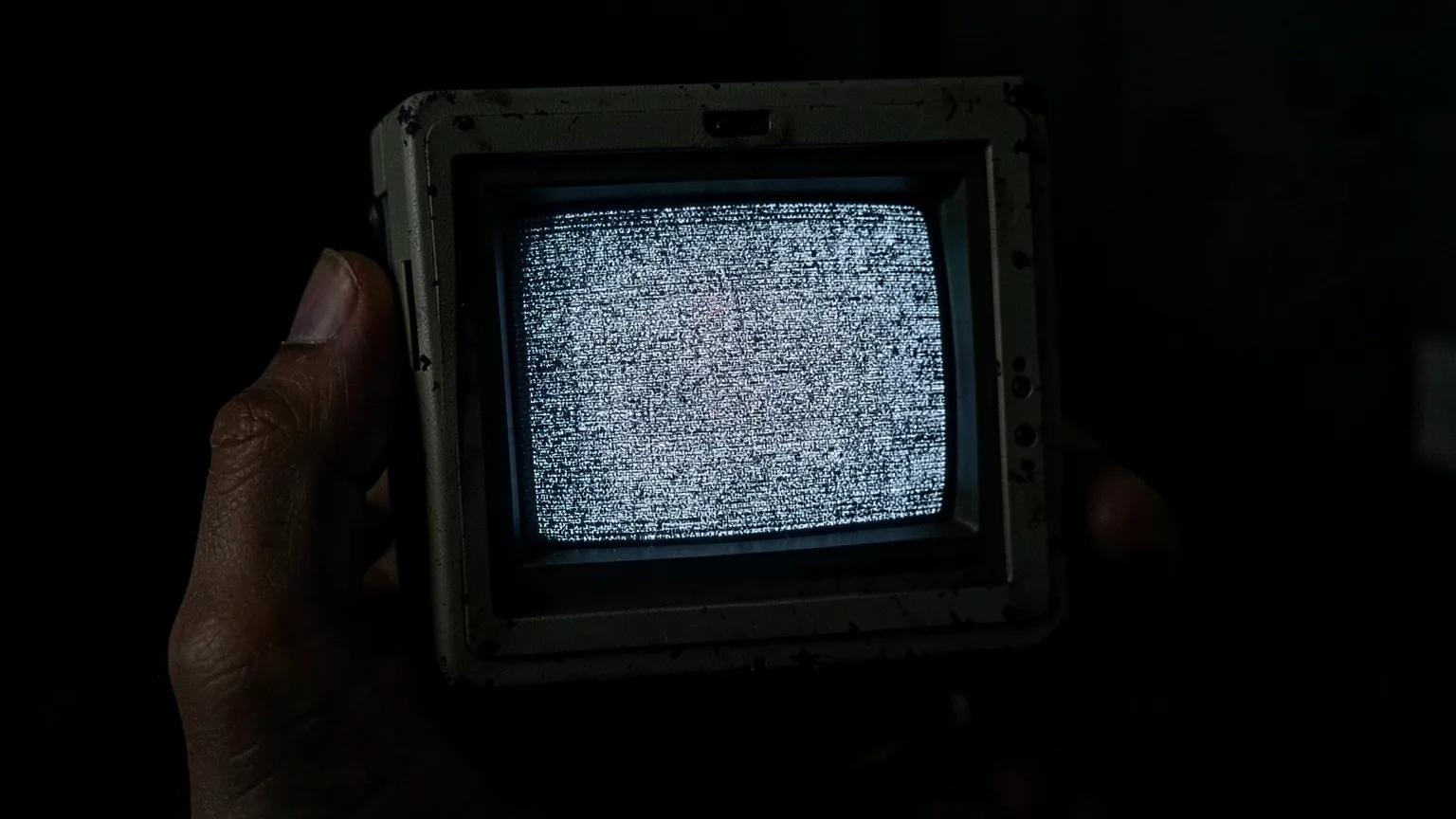 Aparato electrónico antiguo de mano con una pequeña pantalla de tubo encendida con estática gris en una habitación oscura