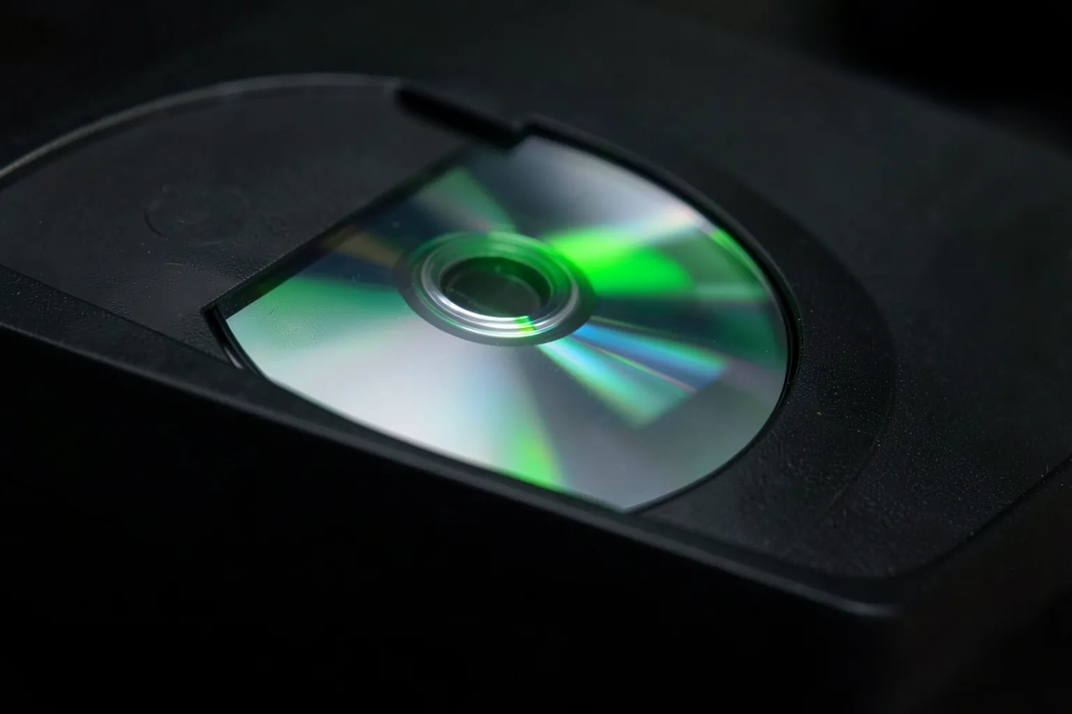 Disco óptico plateado reflejando luz verde junto a la ranura de una consola negra